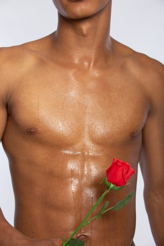 Alex Close-up of a glistening torso holding a red rose, symbolizing passion and strength.